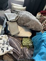 Overview of multiple folded cotton towels with various colors and patterns like stripes and geometric prints on a bed and inside a grey laundry bin.