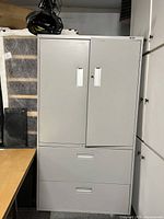 Front view of grey metal storage cabinet showing upper doors and lower drawers.