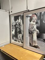 Two large black and white framed photographs of children with pink roses, placed on a wooden surface near white cabinetry.