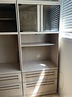 Front-left side view of the light wood display cabinet showing glass display shelves and lower storage drawers.