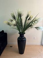 Front side view of tall black ceramic vase with arrangement of artificial green grass, beige pampas grass, and white pom pom stems.