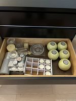 Top view of drawer showing assorted candles, candle holders, mesh decorative balls, clear glass bird figurine, and silver ornaments.