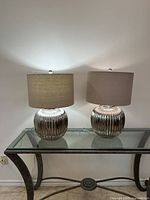 Pair of modern table lamps on glass and metal table against white wall, showing overall appearance and proportions.