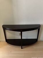 Front view of the walnut wood console table showing its smooth, curved semi-circular structure with two shelves and a central support leg.