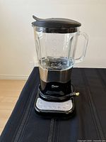 Front view of Oster blender showing glass jar, black and stainless steel base, control buttons on base panel.