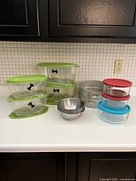 Photo showing all items in the lot including springform pans, metal bowls, and food storage containers on kitchen counter.