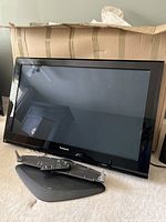 Front view of the Panasonic plasma TV on carpeted floor with stand base and remote placed in front.