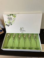 Six Perrier-Jouet branded champagne glasses inside white box with floral design.