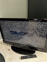 Front view of Samsung 32-inch LCD TV powered on showing 'Weak or No Signal' message, with remote control placed in front.