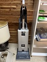 Full view of grey upright vacuum cleaner with attached hose and tools
