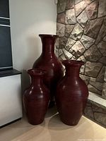 Three large red decorative floor vases of different shapes grouped together showing size and color