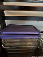 Stack of three clear rectangular Pyrex glass dishes with purple lids on top, showing lids clearly