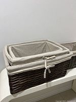 Set of four nested rectangular woven baskets with beige fabric liners, showing dark brown wicker material and fabric ties