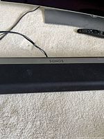 Top view of black Sonos Playbar on carpet showing SONOS logo and cloth grille with minor scratches