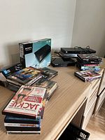 Sony Blu-ray Player BDP-BX110 in original box with stacks of movie DVDs and two other Blu-ray players (Samsung and LG) on wooden surface