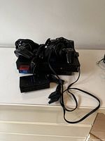 Sony PlayStation 2 console with cables and two controllers, stacked on a white surface.