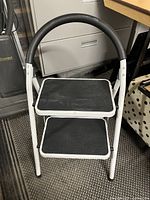 Front view of 2-step folding step stool with black rubber treads and padded handle.