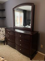 Front view of dark wood dresser with matching arched mirror against grey wall