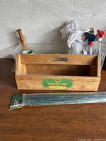 Vintage wooden Canada Dry pop carrier box with green label and some graffiti marks, shown on wooden table with background containing cleaning supplies.