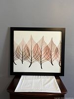 Front view of square framed wall art with black frame and brown translucent leaf design on white background.