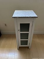 Front view of a small white cabinet with gray granite top and frosted glass panel door, displayed against wall.