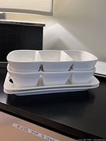 Stacked white ceramic serving trays divided into three sections each, with raised edges and flat base