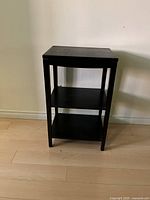 Front view of the black wooden side table with three shelves, showing overall condition and structure.
