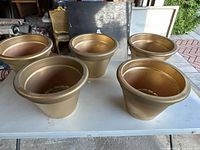 Five gold-colored clay pots arranged on a white table, showing the outward appearance and shape.