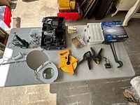 Photo shows assorted hardware and tools on a gray table including clamps, measuring tape, light fixtures, and inspection camera in carrying case.