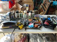 Overview of table with assorted tools including spray paint cans, power tools, hand tools, and tool cases.