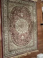 Full view of the rectangular carpet showing the central medallion and the intricate pattern in wine, cream, and beige colors on a hardwood floor.
