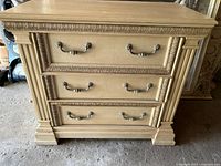 Front view of the dresser showing three drawers, ornate metal handles, and carved decorative trim around drawers and top.