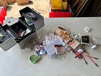 Eyelash extension kit elements spread on a table around a black foldable organizer box, showing eyelash trays, adhesive tubes, spoolies and other small tools