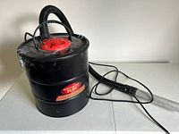 Front side view showing the black cylindrical metal body, red motor cover on top and hose with extended nozzle attached.