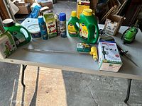 Photo showing a variety of garden supplies on a table including fertilizers, insecticide spray, garden sprinkler, and metal rods.