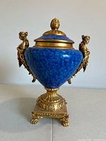 Front view of blue and gold urn showing the figurine handle on the left side.
