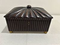 Closed view of the dark wood jewelry box with ridged design, round knob on lid, and brass ball feet
