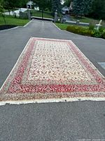 Full rug displayed outdoors on pavement showing red border and ivory field