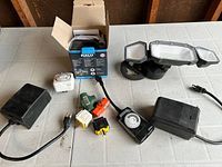 Overview of all items including outdoor motion sensor flood light, electrical timers, plug adapters, transformers on a table.