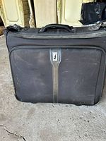 Front view of the black London Fog garment bag showing metal logo badge and fabric front pocket.