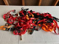 Pile of multi-colored load straps with hooks and ratchets on a grey plastic table.