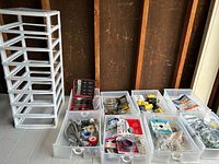 Overview of seven or more clear plastic bins filled with assorted small hardware pieces and plumbing fittings organized on a table beside the shelving unit
