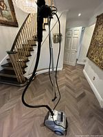 Full view of the garment steamer with hose and base on wooden floor near staircase.