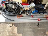 Overall display of bench grinder, hose, clamps, drill bits, paint brushes and other tools on a table.
