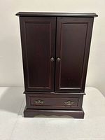 Closed view of the small wooden jewelry box with two front doors and a drawer at the bottom.