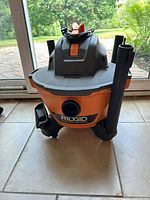 Front view of an orange and black Ridgid small shop vacuum with power switch and attachments.