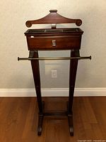 Full front view of the dark wooden suit valet stand showing hanger, drawer, tray compartments, metal pant bar, and base feet.