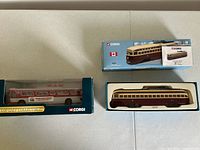 Three diecast models in boxes on tabletop: streetcar top right, bus bottom left, another streetcar bottom right