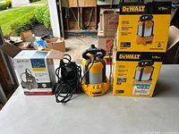 Two submersible pumps on table with packaging: yellow and black DeWalt pump and black Burcam pump with boxes.
