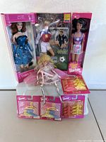 Lot of three boxed Barbie dolls, one loose doll, and three unopened sets of Barbie doll hangers displayed on table